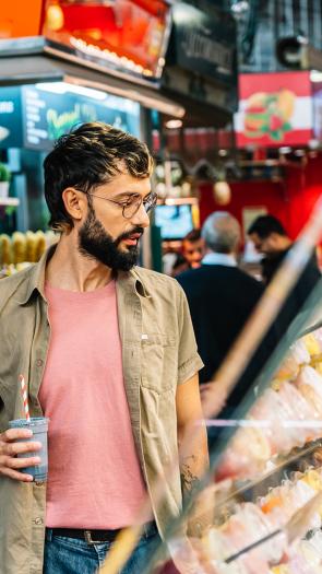 Man met bril en blauwe smoothie kijkt naar vitrine met soorten gebak