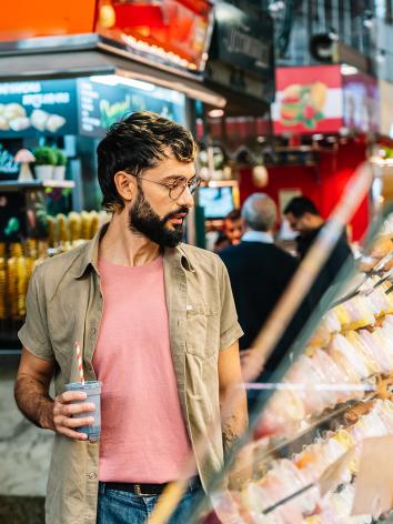 Man met bril en blauwe smoothie kijkt naar vitrine met soorten gebak