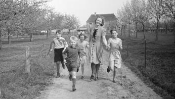 een zwart-wit foto van een moeder met vier kinderen bij een boerderij