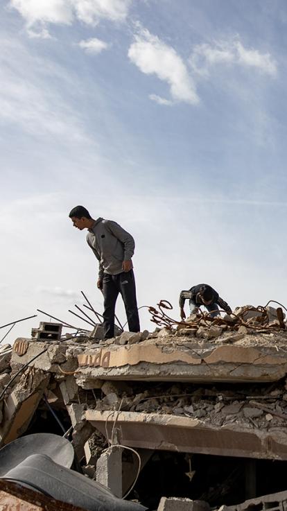 Jongens zoeken door puin van een gebombardeerde woning