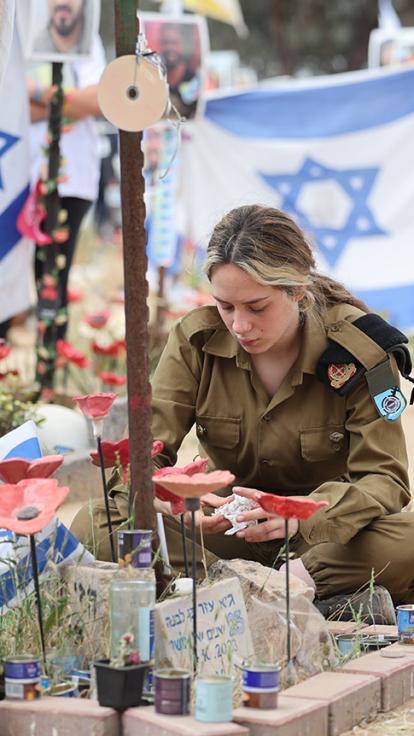 Vrouw in Israëlisch legeruniform bij graf op herdenk plaats 7 oktober 2023