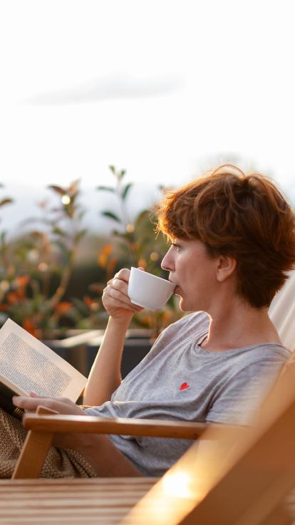 Een dame die in de zon thee drinkt en een boek leest 