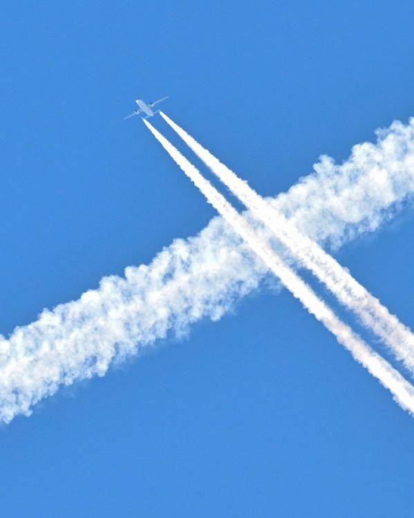 een vliegtuig laat witte strepen achter in de blauwe lucht