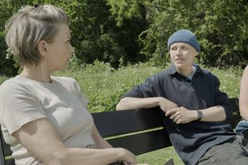 Nout van leven tot het laatst zit op een bankje in gesprek met Anita Witzier omringt door groene bomen en groen gras