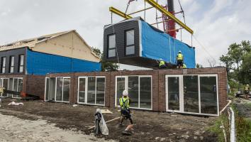 Een hijskraan zet een kant en klare kamer bovenop de onderste verdieping van een nieuw huis.