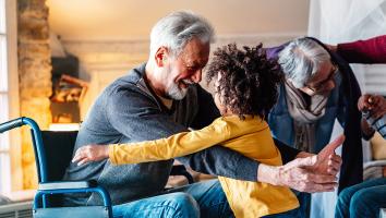 Grootouders met 2 kleinkinderen. Opa in rolstoel geeft een van de kinderen een knuffel
