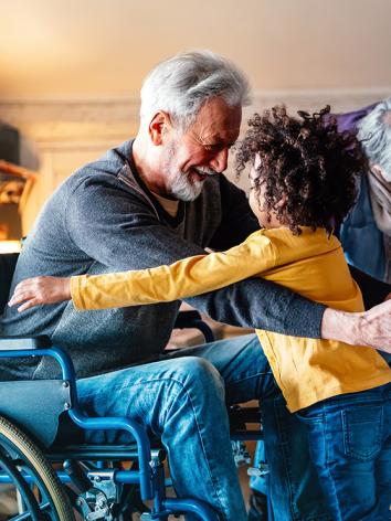 Grootouders met 2 kleinkinderen. Opa in rolstoel geeft een van de kinderen een knuffel