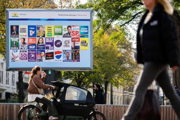 burgers fietsen langs een campagnebord op straat met alle verkiezingsposters erop