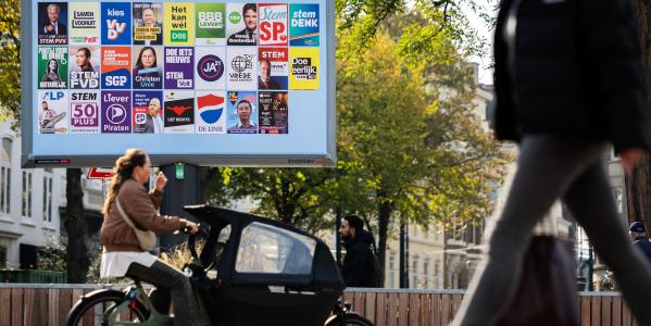 burgers fietsen langs een campagnebord op straat met alle verkiezingsposters erop