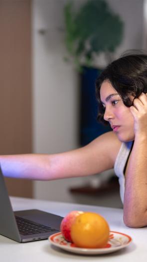 Vrouw zit aan tafel achter laptop. Houdt laptopscherm vast en kijkt bedroefd. 