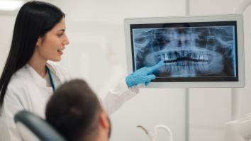 Tandarts met medische handschoen wijst naar röntgenfoto van gebit met man in tandartsstoel ernaast