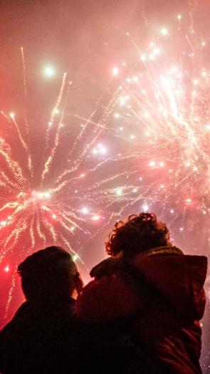 een ouder met kind in de armen bewondert het siervuurwerk in de lucht