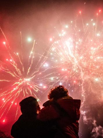 een ouder met kind in de armen bewondert het siervuurwerk in de lucht