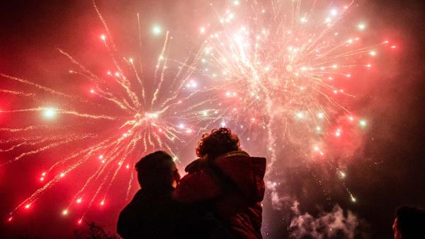 een ouder met kind in de armen bewondert het siervuurwerk in de lucht