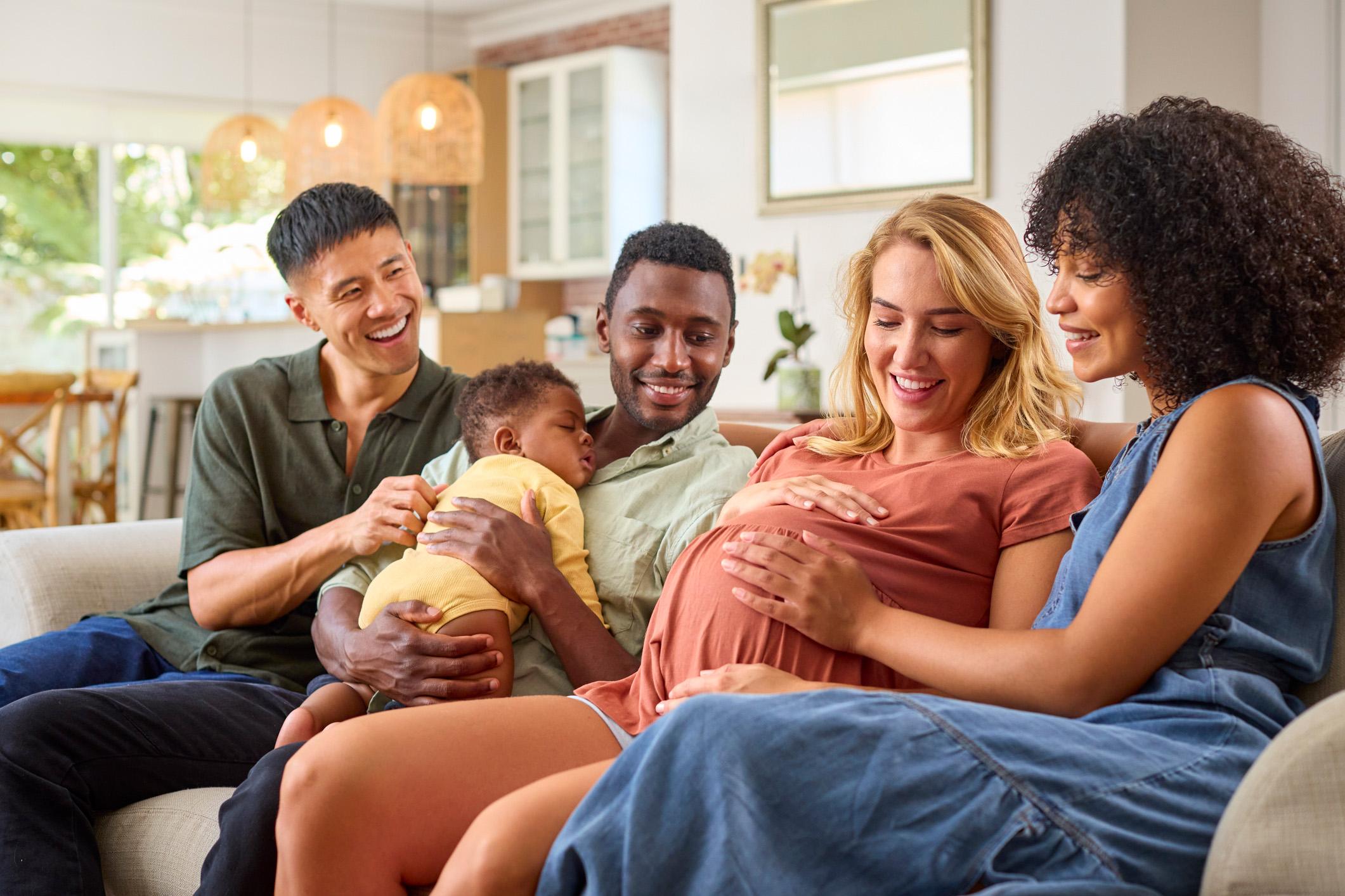 Twee stellen zitten samen op de bank met hun kind en een van de vrouwen is zwanger.
