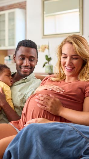 Twee stellen zitten samen op de bank met hun kind en een van de vrouwen is zwanger.