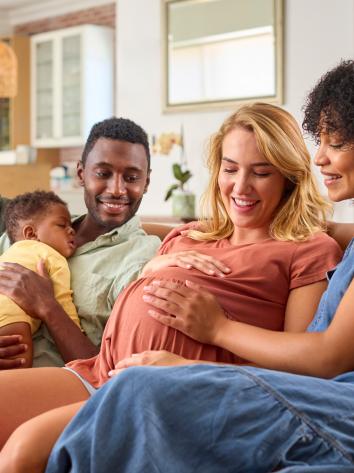 Twee stellen zitten samen op de bank met hun kind en een van de vrouwen is zwanger.