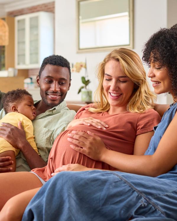 Twee stellen zitten samen op de bank met hun kind en een van de vrouwen is zwanger.