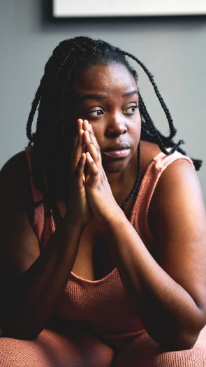 een vrouw staart voor zich uit met haar handen ineen gesloten