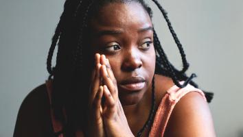 een vrouw staart voor zich uit met haar handen ineen gesloten