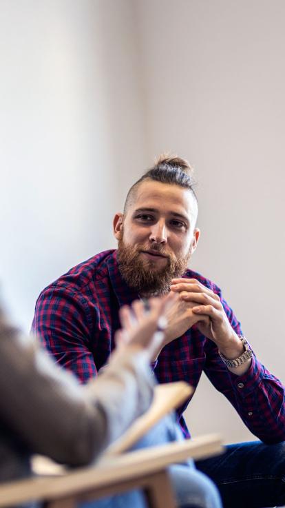 Een foto van een cliënt die aandachtig en glimlachend luistert naar zijn behandelaar bij een therapiesessie.