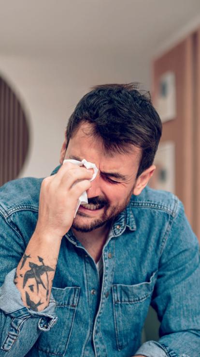 Een foto van een huilende man die zijn tranen wegveegt met een tissue.