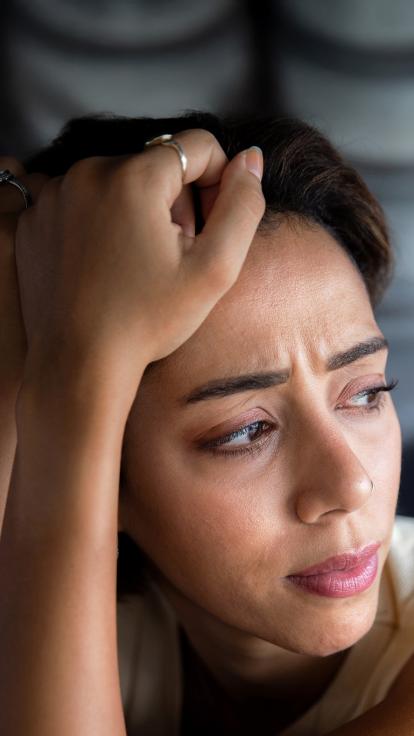 Een vrouw houdt haar hoofd in haar handen terwijl ze somber voor zich uitkijkt. 