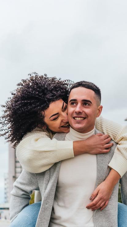 Een foto van een lachend stel. De vrouw zit op de rug van de man terwijl ze elkaar omhelzen.