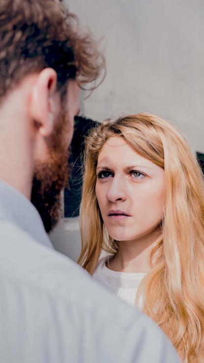 Foto van een vrouw die gespannen en intens naar haar partner kijkt die met zijn rug naar de camera staat.