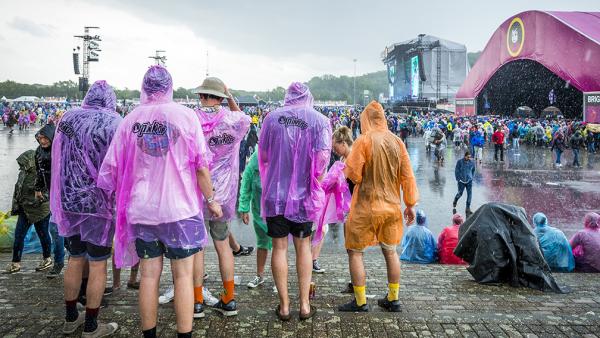 Festivalgangers lopen door de regen op weg naar een concert.