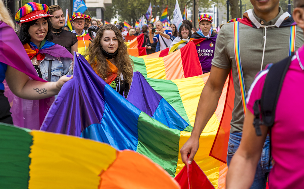 Mensen vieren Gay Pride in Amsterdam met regenboogvlaggen en vrolijke kleding.