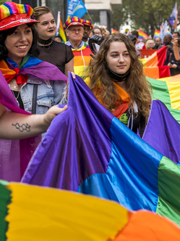 Mensen vieren Gay Pride in Amsterdam met regenboogvlaggen en vrolijke kleding.