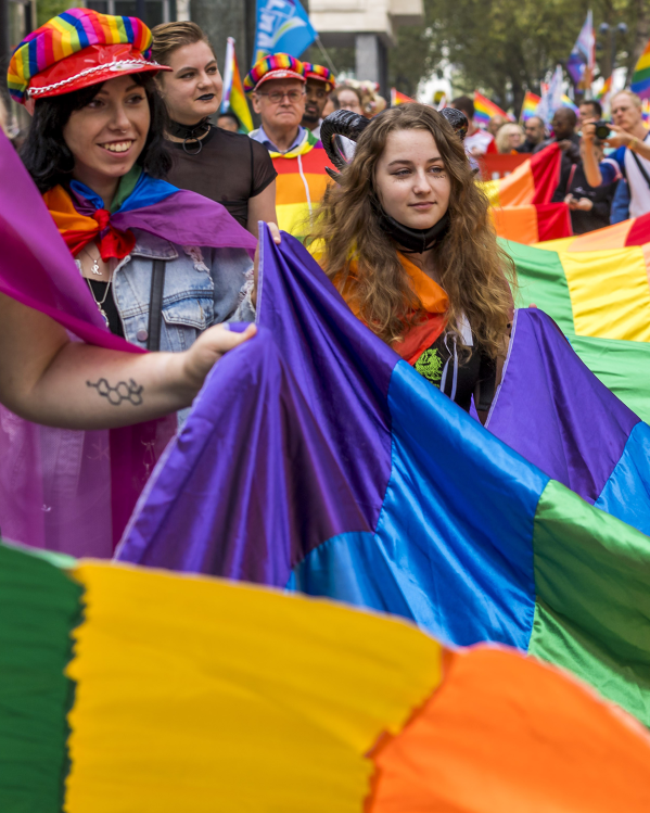 Mensen vieren Gay Pride in Amsterdam met regenboogvlaggen en vrolijke kleding.