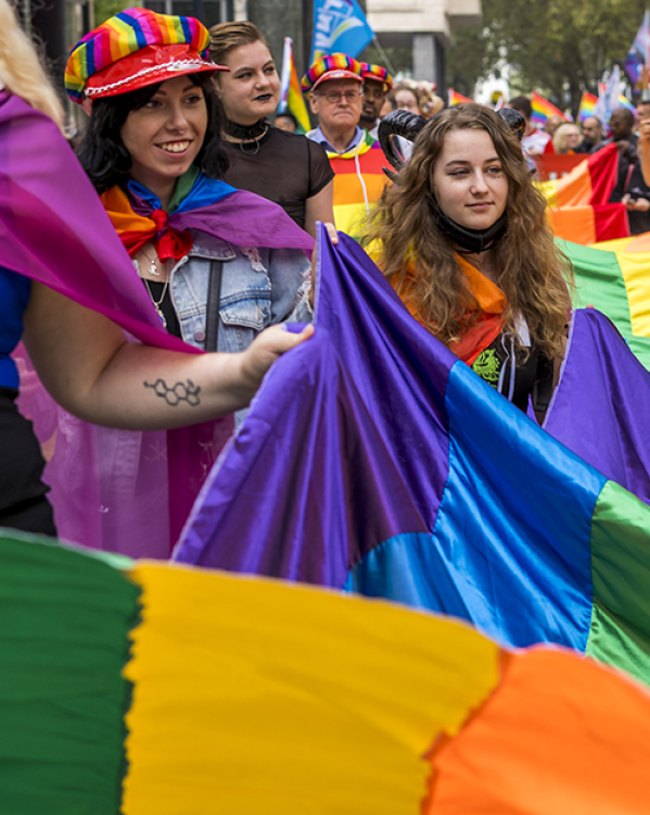 Mensen vieren Gay Pride in Amsterdam met regenboogvlaggen en vrolijke kleding.