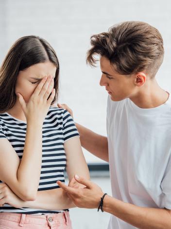 Een foto van een jonge man die een verdrietige jonge vrouw troost door een hand op haar schouder te leggen en haar aan te kijken.