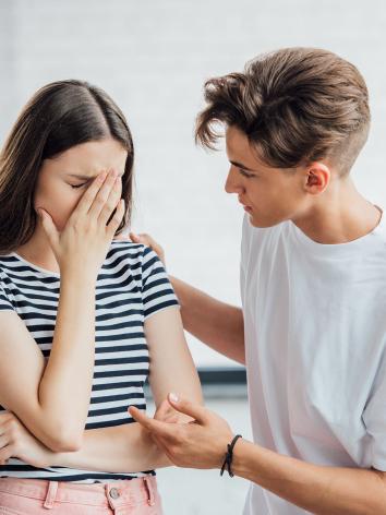 Een foto van een jonge man die een verdrietige jonge vrouw troost door een hand op haar schouder te leggen en haar aan te kijken.