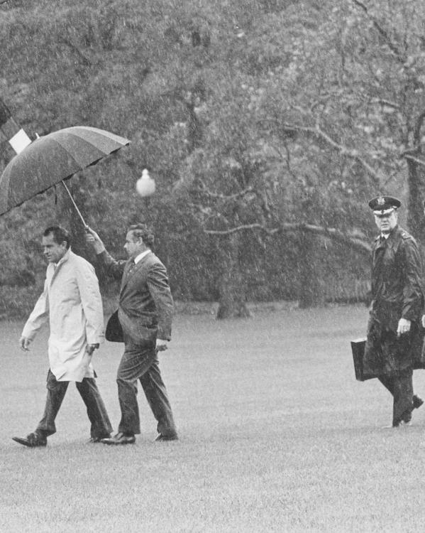 Een zwart-witfoto van president Nixon die naar zijn vliegtuig loopt. Achter hem loopt een militair met het koffertje. 