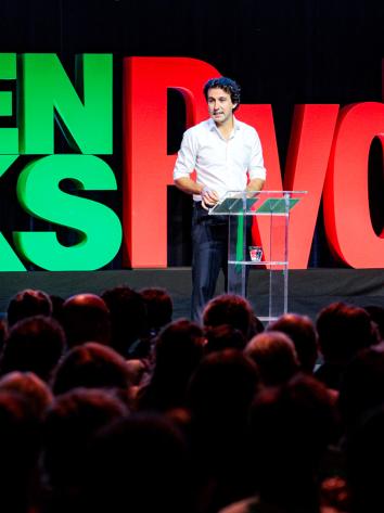 Een foto van politicus Jesse Klaver die op een podium een toespraak geeft voor een groep mensen op het partijcongres van GroenLinks-PvdA. Achter hem staan de letters 'GroenLinks-PvdA' heel groot. 