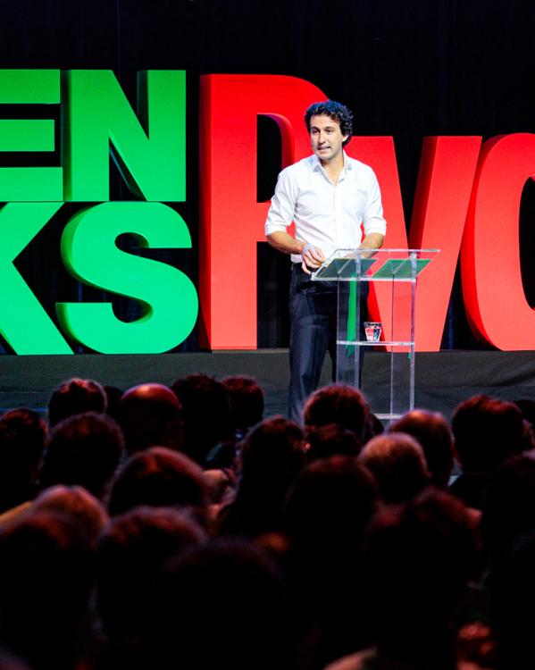 Een foto van politicus Jesse Klaver die op een podium een toespraak geeft voor een groep mensen op het partijcongres van GroenLinks-PvdA. Achter hem staan de letters 'GroenLinks-PvdA' heel groot.
