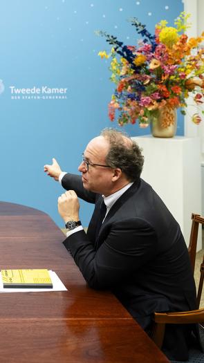 Verkenner Koolmees zit met Caroline van der Plas aan houten tafel in gesprek bij muur waar Tweede Kamer op staat