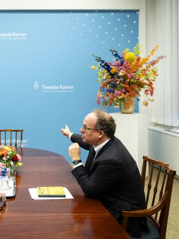 Verkenner Koolmees zit met Caroline van der Plas aan houten tafel in gesprek bij muur waar Tweede Kamer op staat