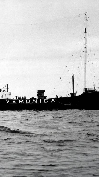 Een zwart-witfoto van het schip van radio Veronica op zee. Op het schip staat in grote letters 'Veronica'. 
