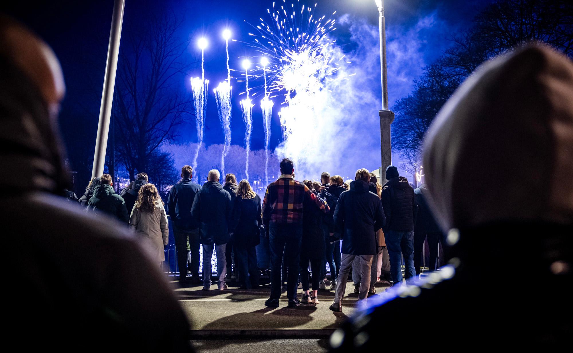 Mensen (met de rug naar de camera) kijken op Oudejaarsavond naar vuurwerk dat wordt afgestoken.