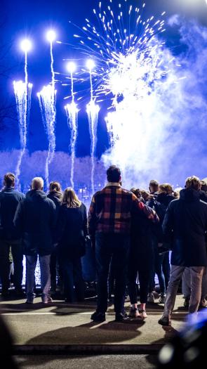 Mensen (met de rug naar de camera) kijken op Oudejaarsavond naar vuurwerk dat wordt afgestoken.