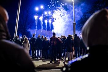 Mensen (met de rug naar de camera) kijken op Oudejaarsavond naar vuurwerk dat wordt afgestoken.