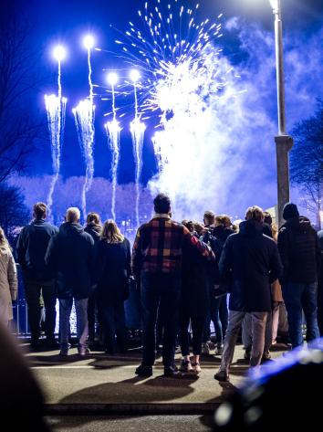 Mensen (met de rug naar de camera) kijken op Oudejaarsavond naar vuurwerk dat wordt afgestoken.