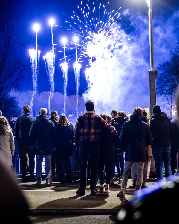 Mensen (met de rug naar de camera) kijken op Oudejaarsavond naar vuurwerk dat wordt afgestoken.