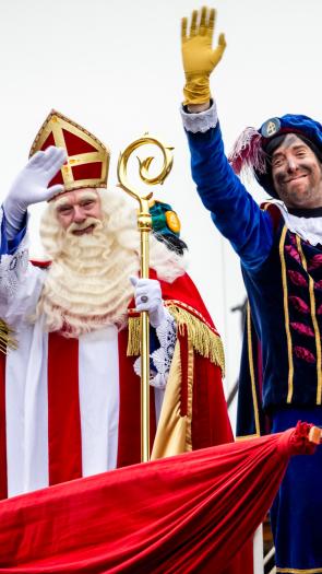 Een foto van Sinterklaas en roetveegpiet die vanaf de pakjesboot zwaaien.