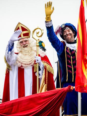 Een foto van Sinterklaas en roetveegpiet die vanaf de pakjesboot zwaaien.