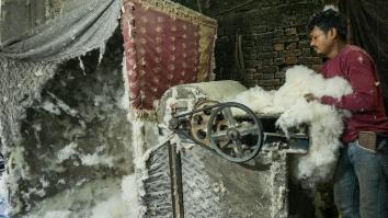 Man stop een hoop pluis van de katoenplant in een machine om het uiteindelijk te kunnen verwerken